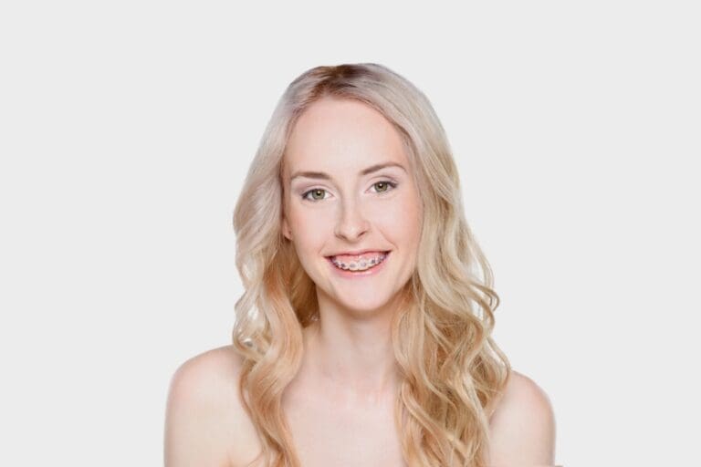 A smiling girl holds and points to an Invisalign Teen aligner with Carpinello Orthodontics in Drexel Hill, Newtown Square or Edgmont, PA, on a blue background.