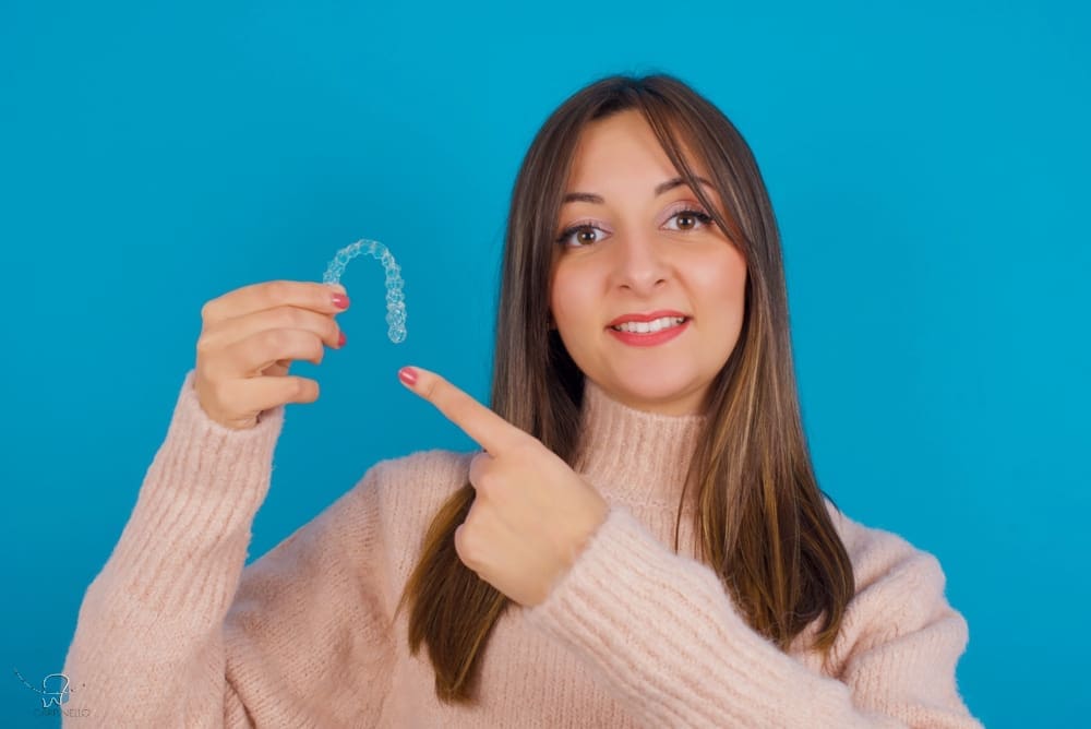 A smiling girl holds and points to an Invisalign Teen aligner with Carpinello Orthodontics in Drexel Hill, Newtown Square or Edgmont, PA, on a blue background. A smiling girl holds and points to an Invisalign Teen aligner with Carpinello Orthodontics in Drexel Hill, Newtown Square or Edgmont, PA, on a blue background.