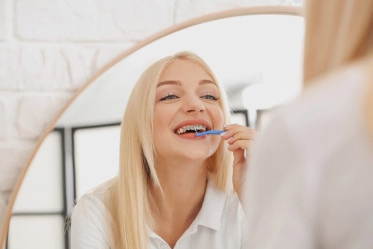 young woman metal braces toothbrush home - How to Floss with Braces in Drexel Hill, Newtown Square, and Edgmont, PA