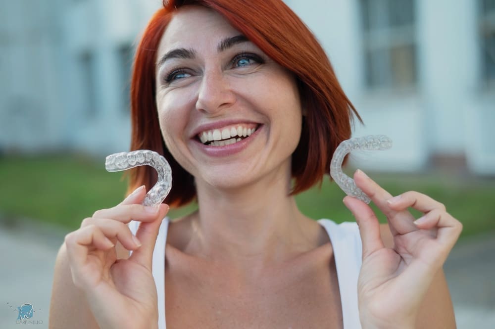 red haired caucasian woman holding transparent invisalign clear aligners for  bite correction - Alternatives to Braces in Drexel Hill, Newtown Square, and Edgmont, PA. 