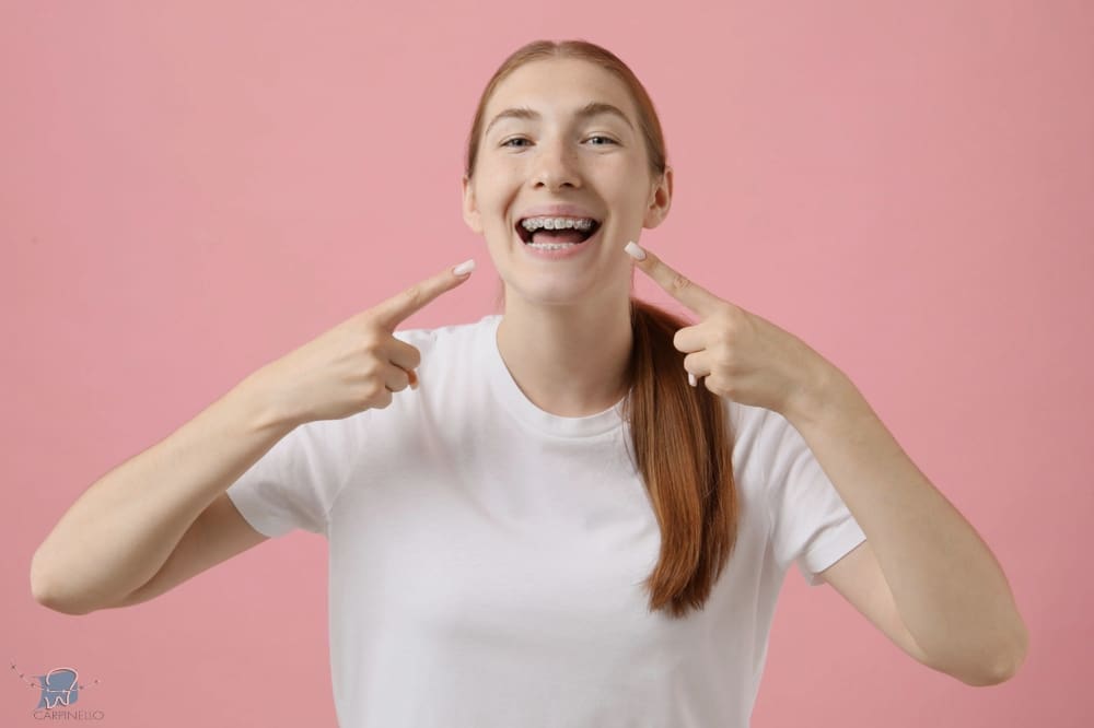 girl pointing her metal braces pink background - How To Get Braces Glue Off Teeth in Drexel Hill, Newtown Square and Edgmont, PA